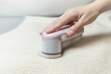 Fototapeta premium Machine for removing pellets from a woolen white jacket. A hand holds a reel removal machine close up photo