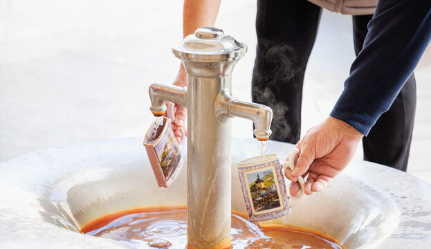 Zwei Personen Rentner f&uuml;llen hei&szlig;es Heilwasser aus einem Thermalbrunnen in traditionell verzierte Kurbecher in einem historischen Kurort Karlovy Vary - Karlsbad, Tschechien 2025-03-27