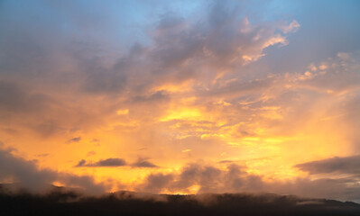 Beautiful sky painted by the sun leaving bright golden shades.Dense clouds in twilight sky in winter evening.Image of cloud sky on evening time.Evening sky scene with golden light from the setting sun