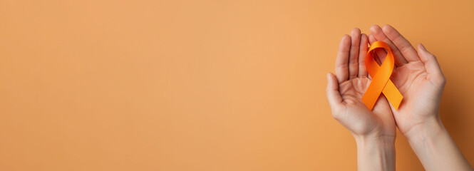 Skin cancer awareness month concept. Hands of woman holding orange color ribbon. Symbolic for Multiple Sclerosis day, self harm awareness, leukemia and kidney cancer. Flat lay, banner, copy space.