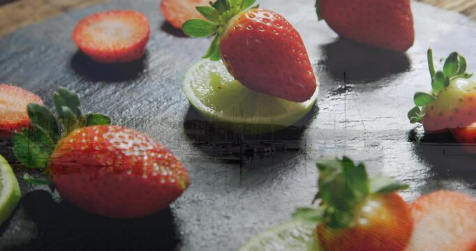 Strawberries and lime slices arranged artistically on dark textured surface