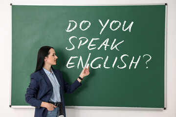 Teacher pointing at phrase Do You Speak English? on green chalkboard in classroom
