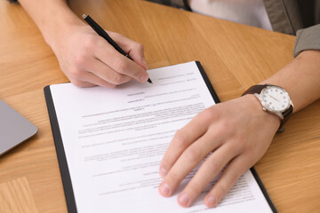 Client signing notarial document at wooden table in office, closeup