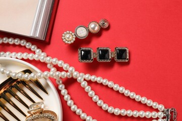 Different hair clips, pearl necklace and comb on red background, flat lay