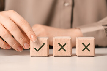 Approved. Woman choosing cube with check mark among other ones with crosses at table, closeup