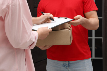 Courier with boxes and receiver signing for delivered parcels indoors, closeup