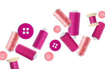 Many sewing threads and buttons in different shades of pink flying on white background