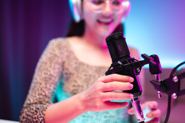 Teenager girl hosts podcast in her room using LED lights, computer, headphones, condenser microphone, tablet to take notes to share knowledge experiences in various fields via live online broadcast.