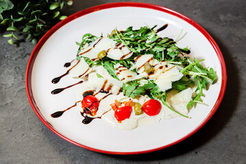 Arugula salad with parmesan and balsamic drizzle. Fresh arugula salad topped with shaved parmesan, cherry tomatoes, capers, and balsamic glaze on a creamy dressing base.