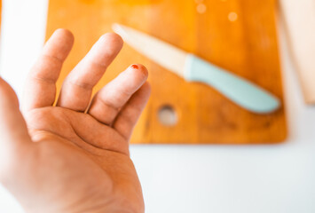 Close-up of a man's  finger cut in blood with a kitchen knife on a background. Injured finger with...