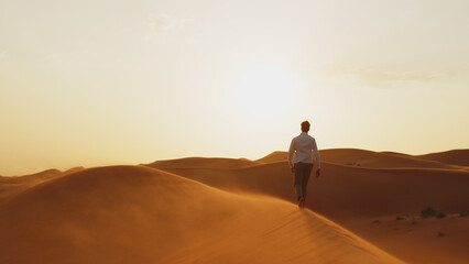 Silhouette of a human walking on the sands in the desert in windy weather while sunrise.  Young man...