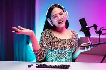 Teenager girl hosts podcast in her room using LED lights, computer, headphones, condenser...