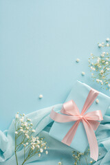 Stylish vertical gift wrapped with a pink ribbon, surrounded by soft fabrics and delicate flowers
