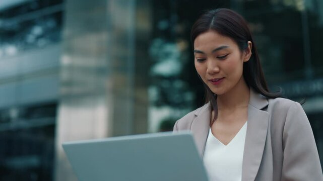 Portrait of Thai woman working on laptop sitting near office building