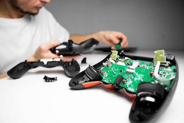 A man in a white shirt repairs a black gaming controller with a small screwdriver. The close-up shot captures his hands and the device against a clean white background.

