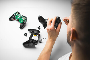 A man in a white shirt repairs a black gaming controller with a small screwdriver. The close-up...