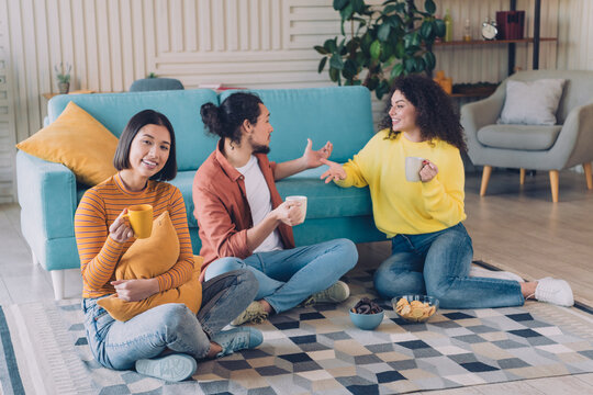 Group of cheerful friends enjoying a casual gathering indoors, having coffee and snacks, sitting in a comfortable living room