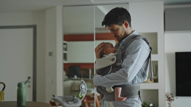 Cinematic portrait of a dad holding his son wrapped in a sling. The young dad cuddles him and gives him kisses. Concept of love, romantic moments, family and father's day