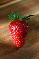 Vibrant strawberry glistening under soft light against wooden surface
