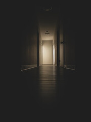Dark and spooky long hallway with light from an open door at the end