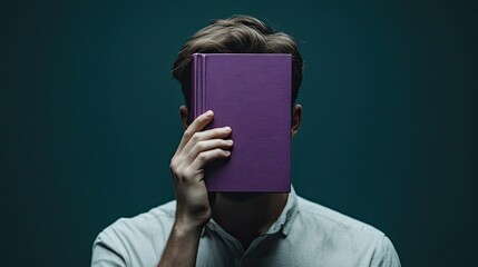 Man covering half his face with a purple book against a dark green background. Concept of deep thought, personal growth, and introspective moments.