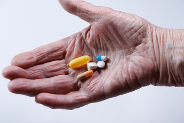 Old woman's hand holding various pills and capsules representing medication and health management