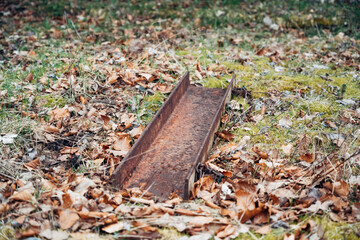 A rusty metal object is laying on the ground in a field of leaves