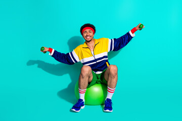 Young sporty man performing workout exercises with a vibrant retro outfit and a cheerful mood against a bright turquoise background.