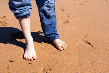 Child feet on sandy beach with rolled up jeans on a sunny day