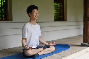 Smiling Young Man Practicing Meditation Indoors on Yoga Mat