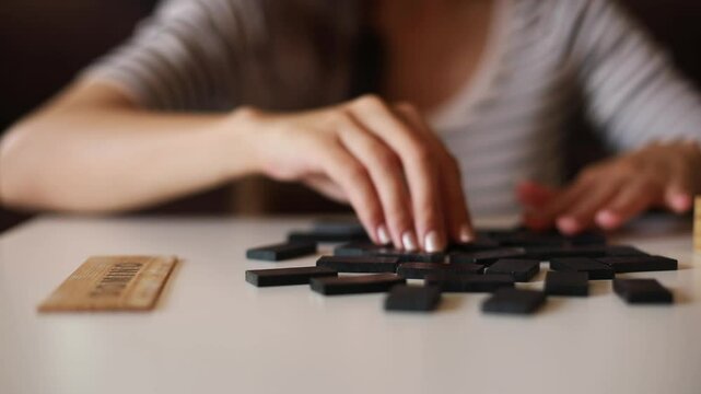 A close-up shot of a hand holding a wooden "DOMINO" tile above a scattered set of black domino pieces. The blurred background and soft lighting create a calm, focused atmosphere.