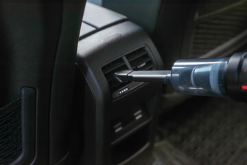 Fototapeta premium Cleaning the air vents of a car with a portable vacuum cleaner