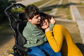 Happy mother hugging son sitting in wheelchair in park