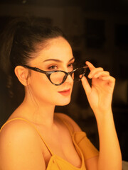 Obraz premium Retro Vintage Portrait of a Woman Adjusting Stylish Glasses in Soft, Warm Lighting With a Nostalgic Atmosphere