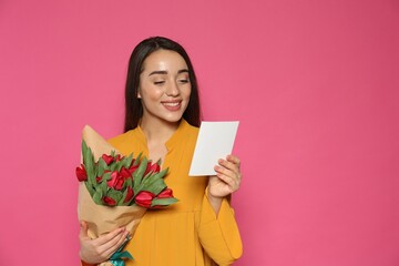 Happy woman with red tulip flowers bouquet reading greeting card on pink background, space for text. 8th of March celebration
