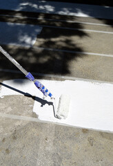 Painting a pedestrian crossing. Painting a zebra crossing. Close-up of a roller painting the white stripes of a pedestrian crossing on the asphalt of a street. Urban signage.