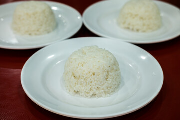 Three servings of white steamed rice, molded into small domes, on white plates. Simple meal staple.