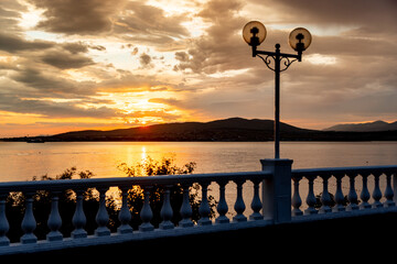 A beautiful sunset over a body of water with a white fence in the background. The sun is setting and the sky is filled with clouds
