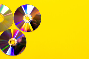 Three colorful compact discs arranged on a bright yellow background reflecting rainbow light...