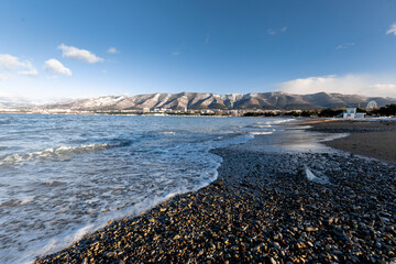 A rocky beach with a body of water in the background. The water is calm and the sky is clear