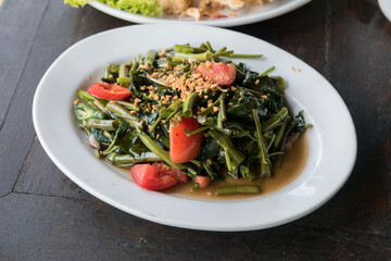 Savory stir-fried water spinach (kangkung) with garlic and chili on a white plate. A simple yet flavorful Southeast Asian vegetable dish.
