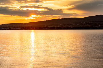 The sun is setting over the water, creating a beautiful orange and pink sky. The water is calm and still, reflecting the colors of the sky. The scene is peaceful and serene