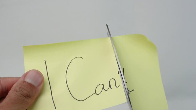 A hand using scissors to cut the words "I Can't" on a yellow sticky note, symbolizing overcoming self-doubt.