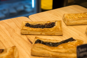 Flaky rectangular pastries with a dark filling, likely fruit or chocolate, displayed on a light wooden surface.