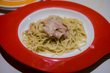 Creamy spaghetti with tuna in a vibrant red bowl. Simple, comforting, and appetizing.