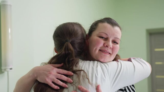 Fair woman filled with joy receives warm welcome hug from healthcare attendant inside clinic room smiling with gratitude before sitting down for her appointment expressing trust in caregiver