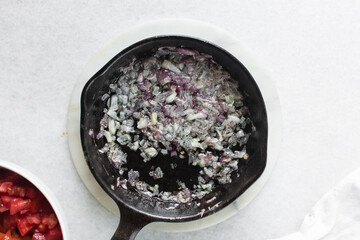 Overhead view of diced onions being sauteed in a cast iron skillet