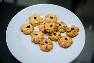 Delicate butter cookies (Semprit Dahlia) arranged on a white plate. These flower-shaped treats often feature a dot of chocolate in the center