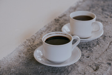 Two cups of bitter black coffee on rough concrete wall background.
