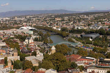 View of Tbilisi showcasing the river, modern architecture, and surrounding hills during a sunny day